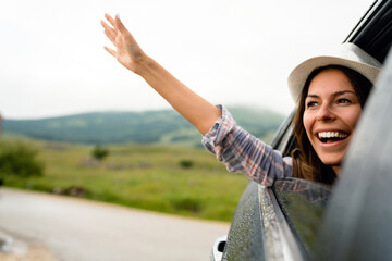 Woman in car road trip waving out the window smiling
