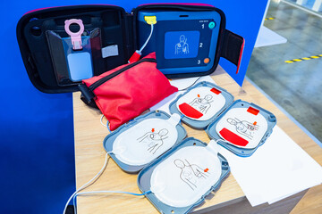 Automatic external defibrillator. Portable defibrillator on a wooden table. Defibrillator for medical care. Device for provision of emergency medical care. Automatic cardioverter with nursing manual - obrazy, fototapety, plakaty