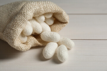 Silk cocoons with sackcloth bag on white wooden table, closeup