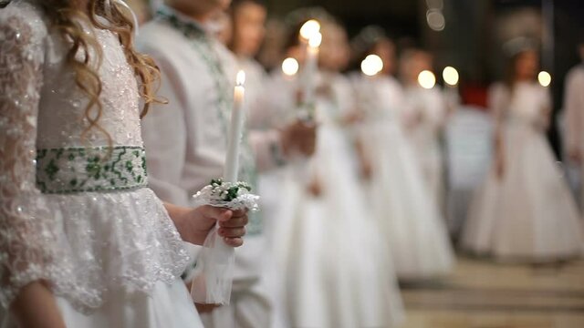 Children stand in church for first communion and hold lighted candles in their hands. - Powered by Adobe
