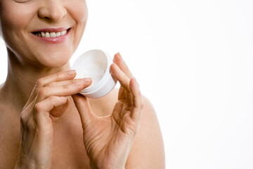 Old woman holding skin care lotion while standing over the white background