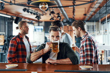 Handsome young man in casual clothing drinking beer while spending time with friends in the pub