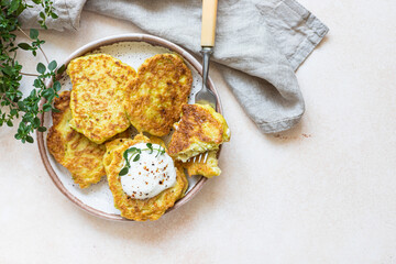 Obraz na płótnie Canvas Vegetable fritters or pancakes with yoghurt or cream sour dressing and herbs. Cabbage or zucchini fritters on ceramic plate. Healthy vegetarian food. Top view.