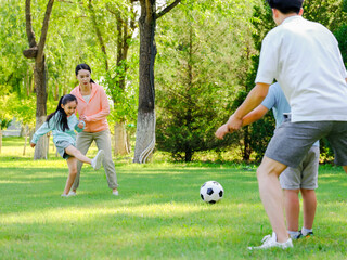 Happy family of four playing football in the park