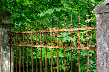 There is an old forged, rusty fence between the concrete pillars.