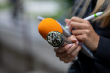 Journalist at news conference, writing notes, holding microphones