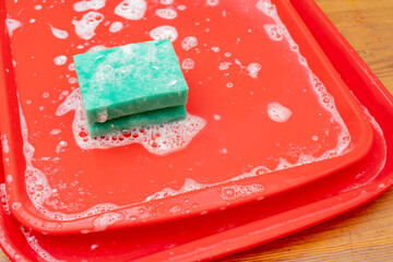 Disinfection of red plastic food tray in fast food. Washing the tray with a sponge and soap.