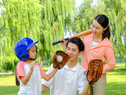 Happy family of three playing baseball in the park