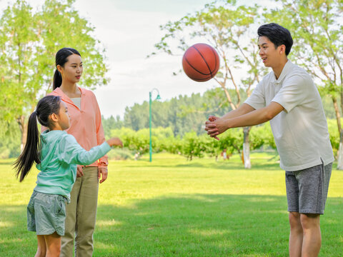 Happy family of three playing basketball in the park