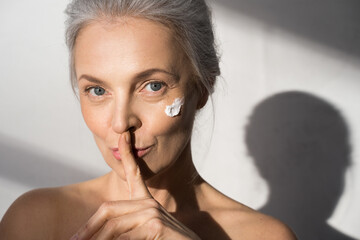 Calm woman with moisturizing cream at her chick putting a finger to her lips