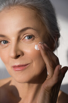 Senior lady receiving moisturizer cream treatment at her skin under the eye