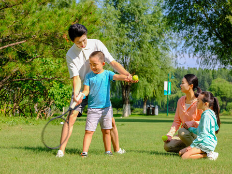 Happy family of four playing tennis in the park