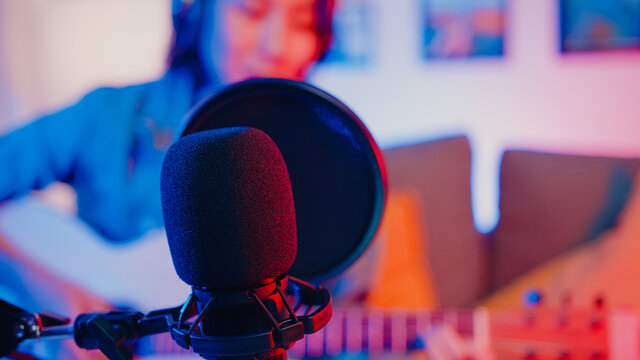 Happy asia girl blogger play guitar and use microphone sing song record music sound mixer on laptop in modern living room home studio at night. Music content creator, Tutorial, Broadcast concept.