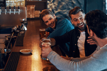 Carefree young men in casual clothing drinking beer and bonding together while sitting in the pub