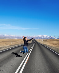 Woman jumps up on empty road on country side, view along Chuysky tract, Altai Republic, Russia