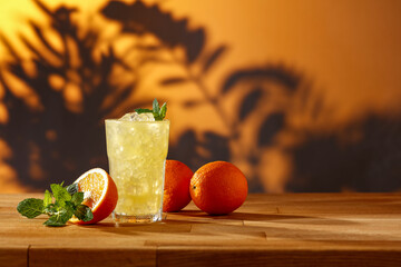 Oranges on the table and a cold drink in a glass with ice in the shade of the leaves and a golden sunset 