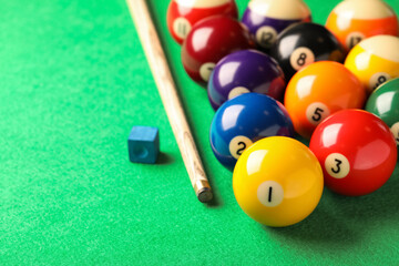 Many colorful billiard balls, cue and chalk on green table. Space for text