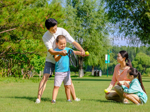 Happy family of four playing tennis in the park