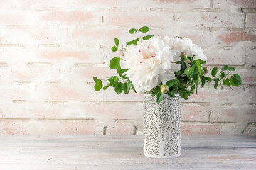 Flower arrangement with white peonies flowers in a vase on a white brick background