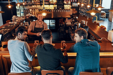 Top view of relaxed young men in casual clothing drinking beer while sitting in the pub