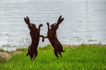 metal sculpture of two hares boxing on the grass by the sea