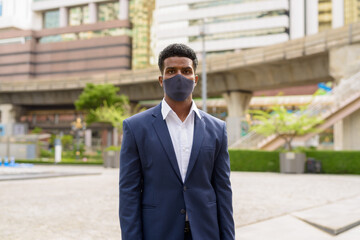 Portrait of African businessman wearing face mask outdoors in city