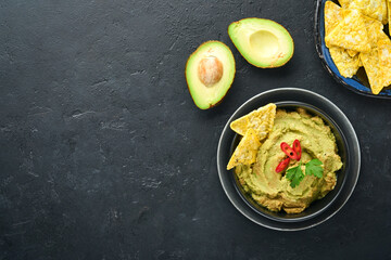 Guacamole. Traditional latinamerican Mexican dip sauce in a black bowl with avocado and ingredients and corn nachos. Avocado spread. Top view. Copyspace
