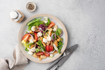 Italian summer salad Panzanella with tomatoes, mozzarella cheese and bread on grey concrete table background, top view, copy space