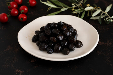 Black olives on a dark background. Tasty black olives in the plate