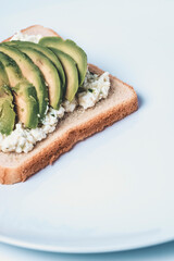 Close-up of a slice with cheese and avocado on a white plate.