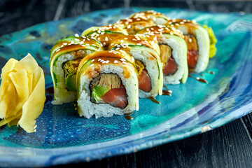 Fresh, Japanese sushi rolls with cucumber, unagi sauce and salmon, served in a blue plate on a dark background. Japanese cuisine