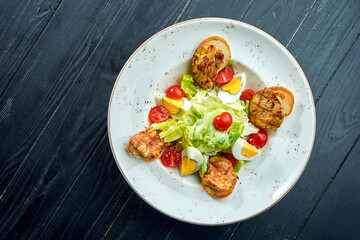 Caesar salad with croutons, parmesan, bacon, chicken, egg in black plate on wooden background. Restaurant serving. Close up with copy space.