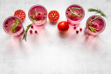 Glasses of cranberry lemonade and red oranges with rosemary