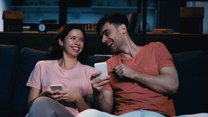 man laughing with woman and holding smartphones in modern living room.