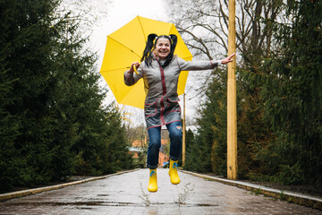 Happy senior cheerful mature, elderly, retired woman with yellow umbrella enjoying life at rainy...