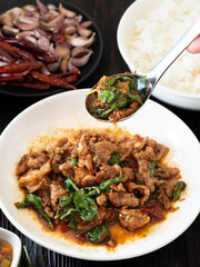 Focus Stir fried pork and basil on spoon and food on brown wooden table background. Favorite food in Thailand.
