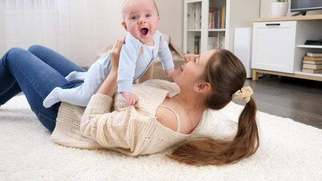 Happy smiling mother with little baby son lying on floor at living room and having fun. Concept of family happiness and child development