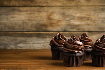 Delicious chocolate cupcakes with cream on wooden table. Space for text