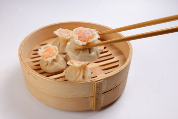 Prawn shrimp shaomai dim sum dumpling in bamboo steamer picked up by chopsticks on white background