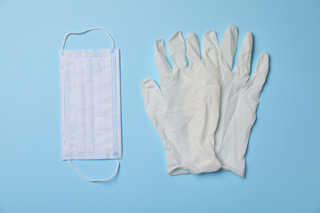 Medical gloves and protective mask on light blue background, flat lay. Safety equipment