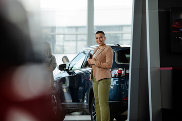 Smiling saleswoman holding tablet while looking at camera at car showroom.