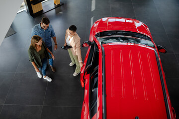 Couple choosing and buying car at car showroom. Car saleswoman helps them to make right decision.