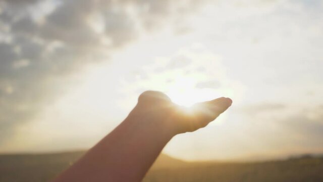 Close-up point of view 4k stock video footage of one female hand raised to morning sunrise sky with soft sun. Sunlight on female cupped palm. Silhouette of hand holding and catching sunshine