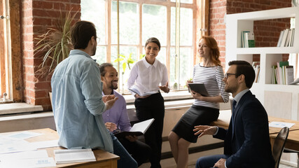 Happy inspired young mixed race colleagues discussing business ideas at brainstorming meeting in modern loft office. Friendly sincere motivated millennial multiracial employees developing project.
