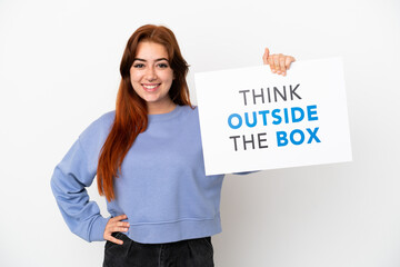 Young redhead woman isolated on white background holding a placard with text Think Outside The Box with happy expression