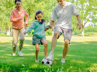 Happy family of three playing football in the park