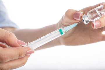 Doctor woman in facial mask medicine dials vaccine into syringe isolated on white background.