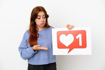 Young redhead woman isolated on white background holding a placard with Like icon and pointing it
