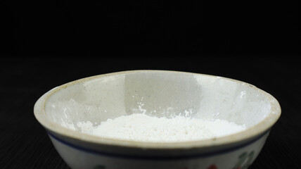 white flour and ceramic bowl on wooden table and black background