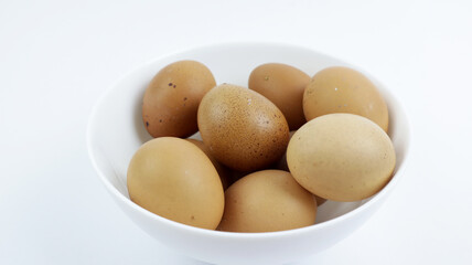 Lots of eggs on a ceramic bowl on a white background. Fresh brown eggs